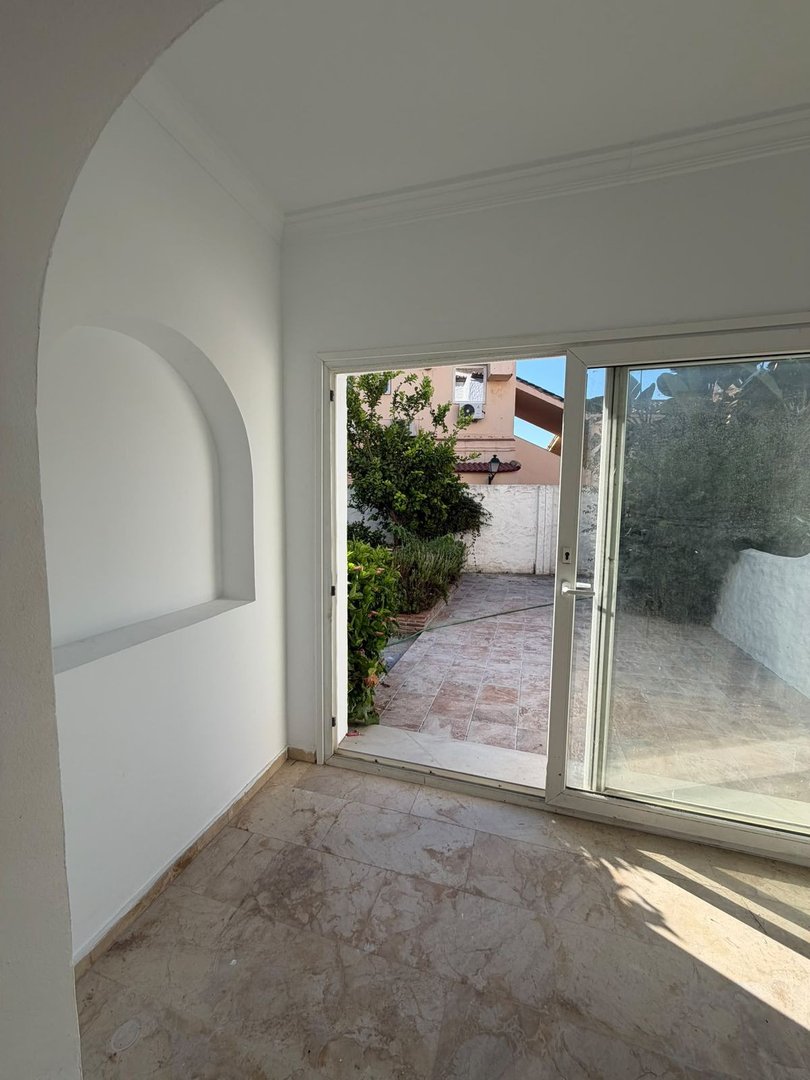 Empty room with sliding glass doors leading to a tiled patio and greenery outside