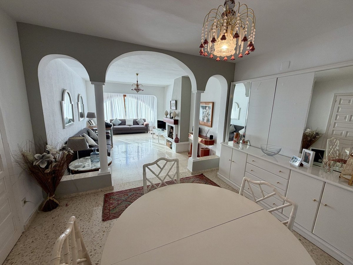 Spacious living and dining area with arched entryways, comfortable sofa, and ornate chandelier, featuring built-in storage and mirrors.