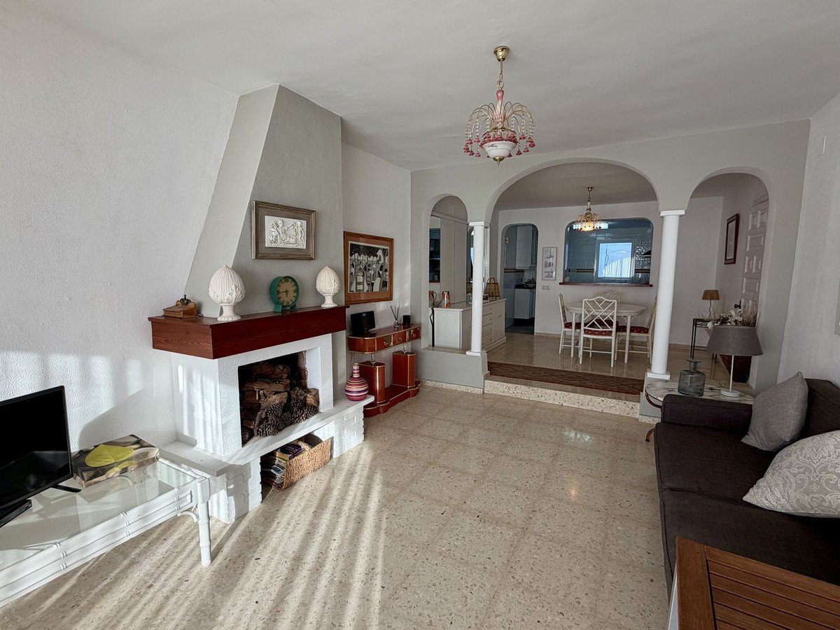 A spacious living room with a fireplace, leading to a dining area with a table and chairs, and a view into the kitchen.