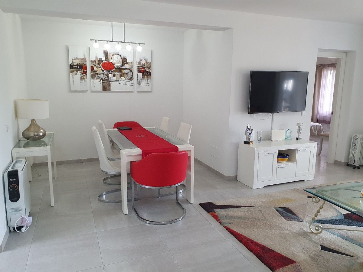 Modern living and dining area with a white table, red chairs, a TV, and abstract art on the wall.