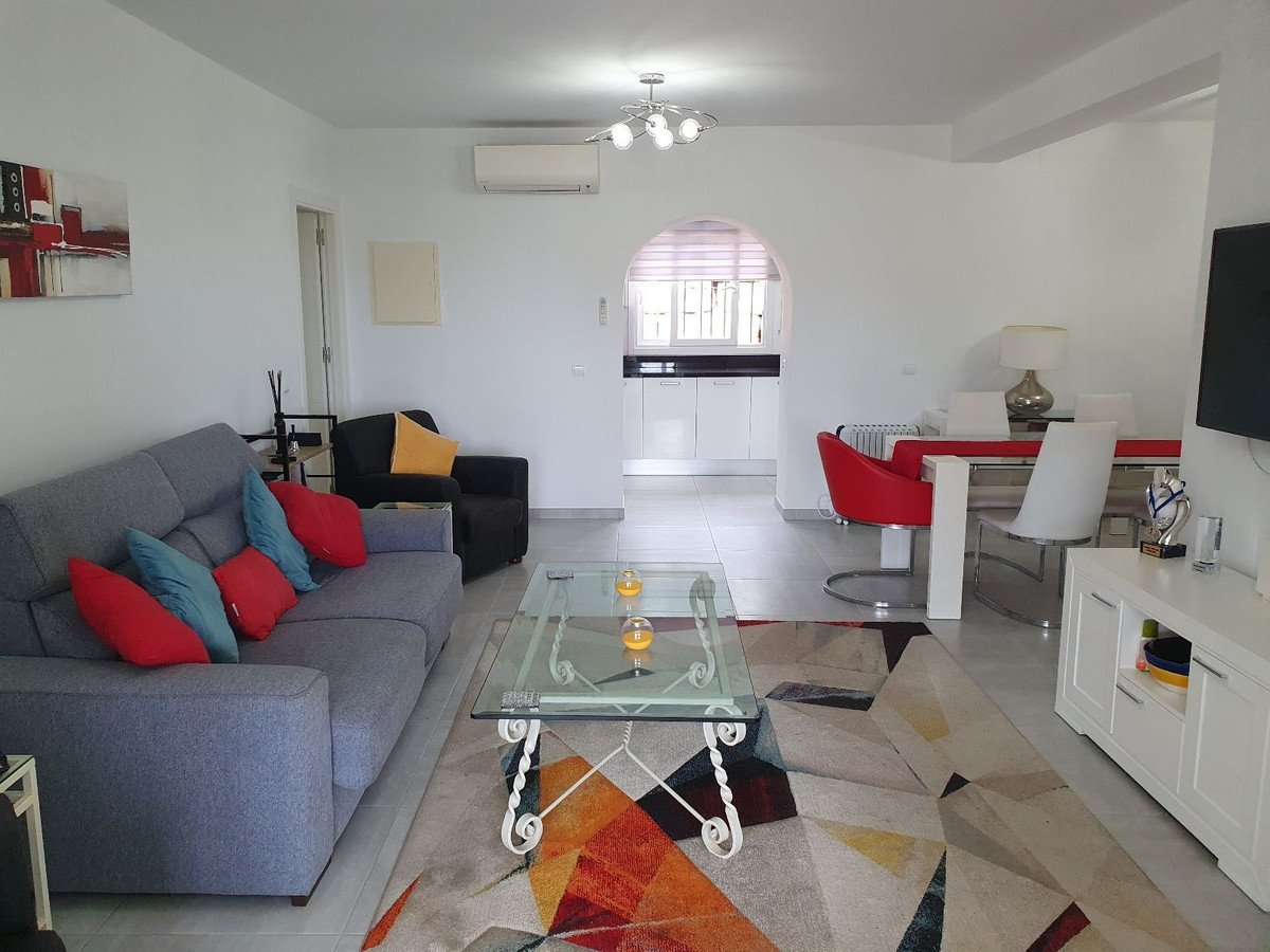 Modern living and dining area with grey sofa, red chairs, and a colorful geometric rug.