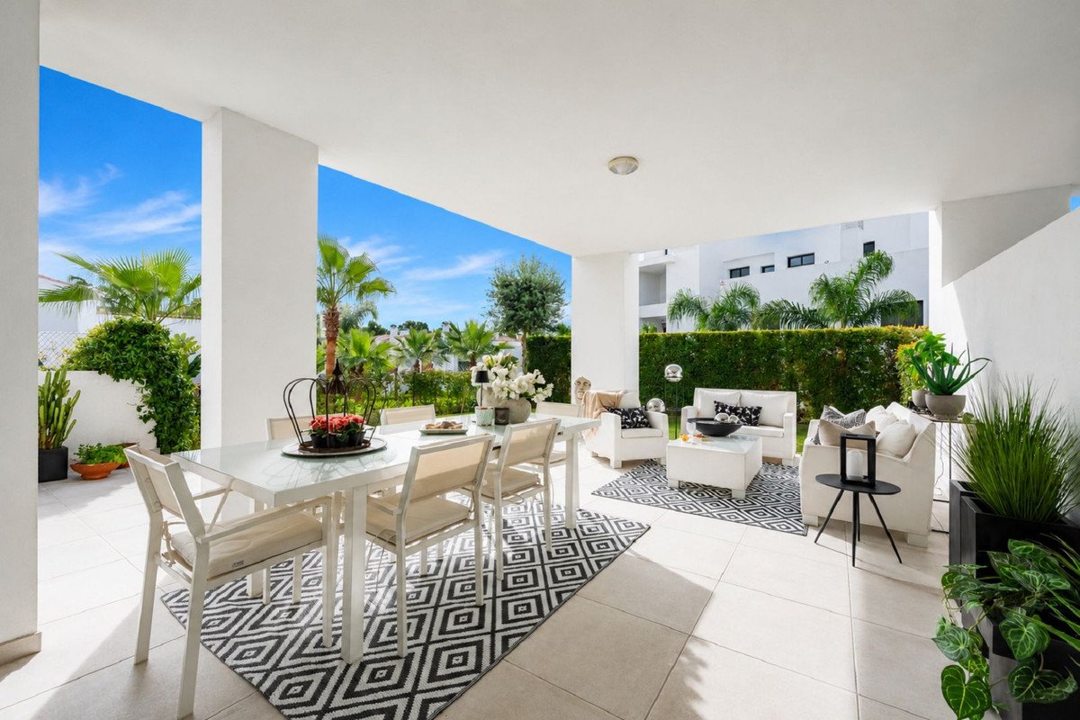 A spacious covered terrace features a white dining table set and a white outdoor sofa set with black and white patterned rugs.