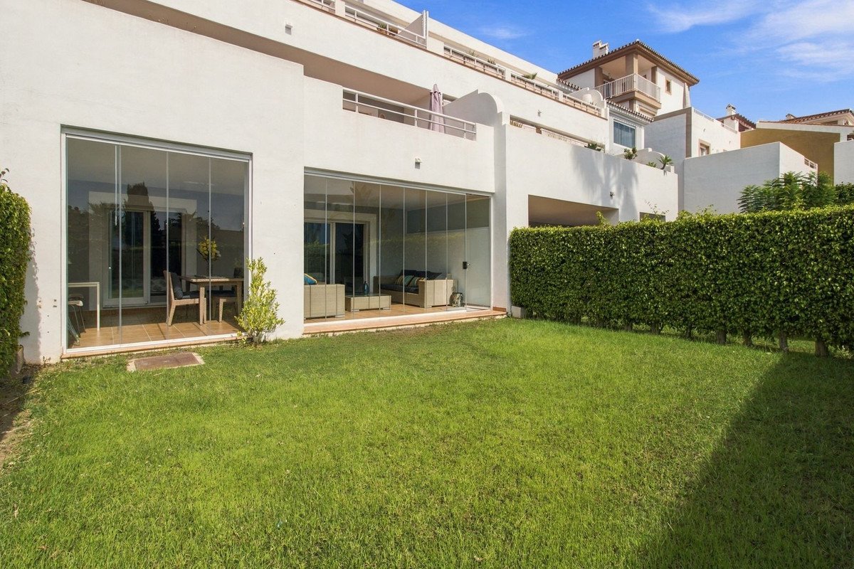 Modern living space with floor-to-ceiling glass doors opening onto a private garden, featuring outdoor seating and dining areas.