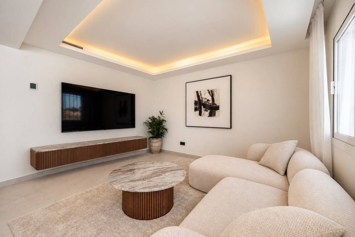 Modern living room with large TV, stylish sofa, coffee table, contemporary artwork, and recessed ceiling lighting.