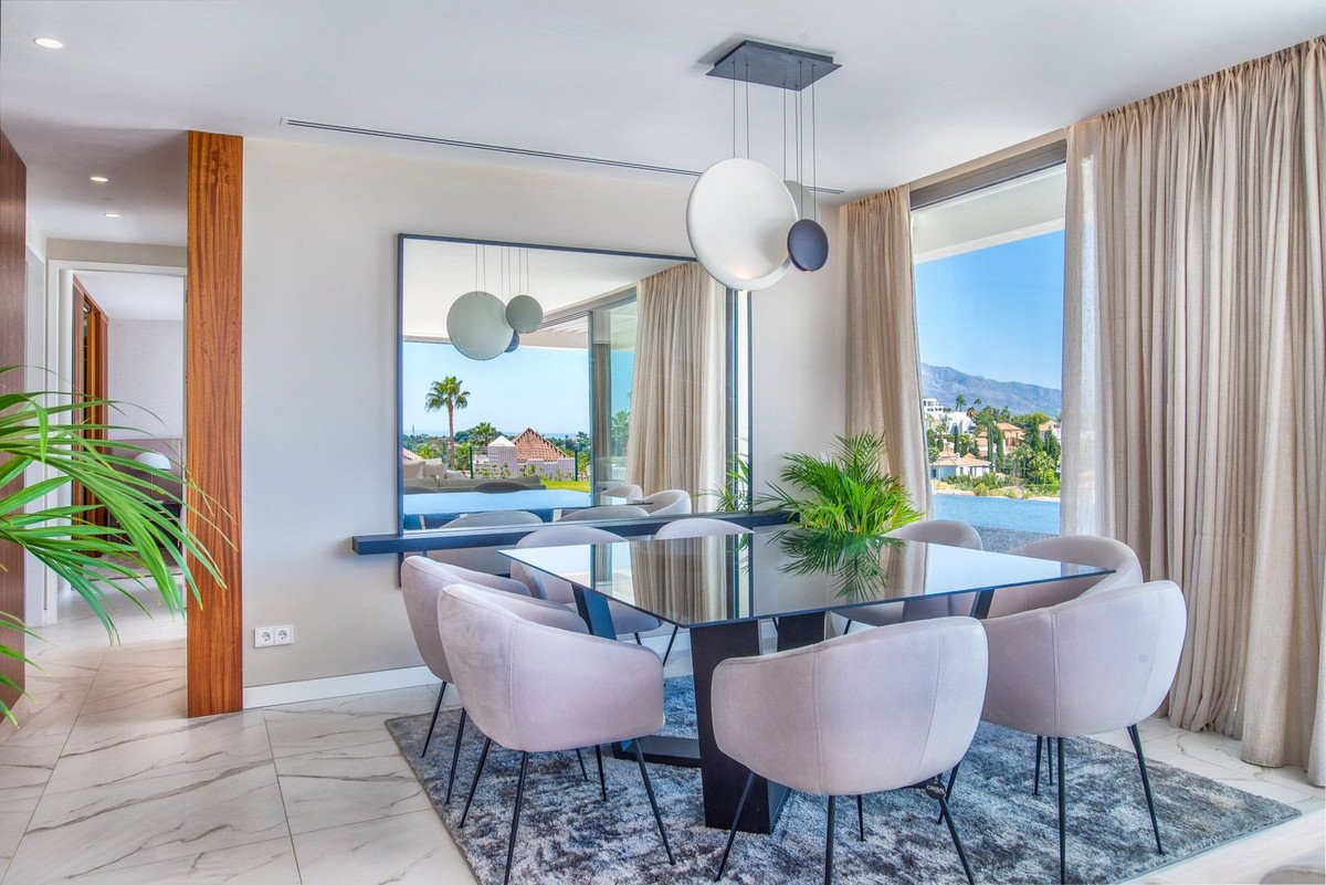 Modern dining room with sea and mountain views, featuring a glass table and plush chairs.