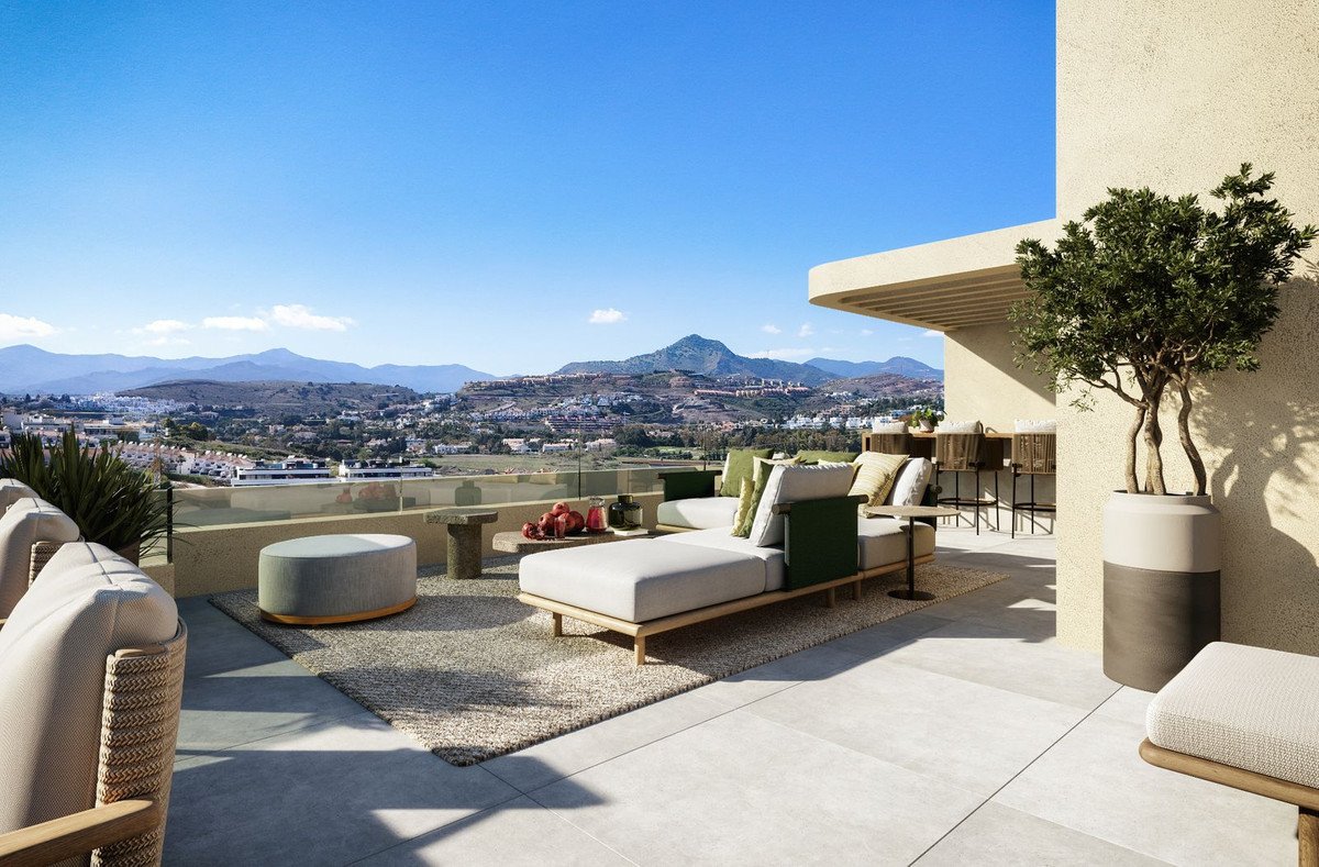 A modern terrace with comfortable seating, a bar area, and panoramic views of mountains and a town.