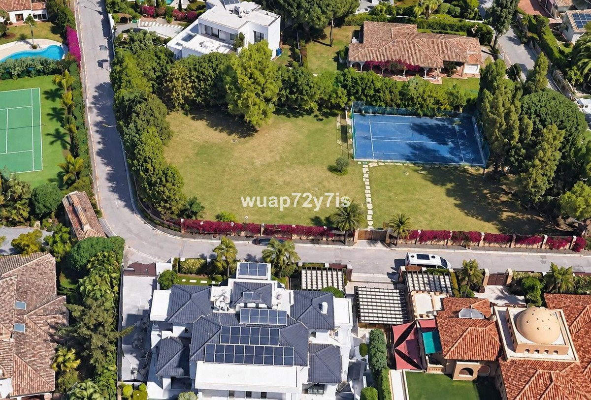Aerial view of a property with a tennis court, swimming pool, and modern villa. Lush green surroundings and trees are visible.