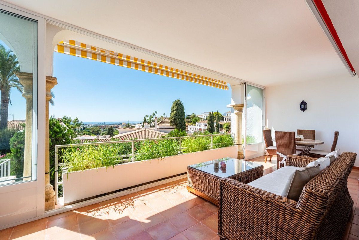 Spacious covered terrace with wicker furniture, dining set, and expansive sea and town views under a sunny sky.