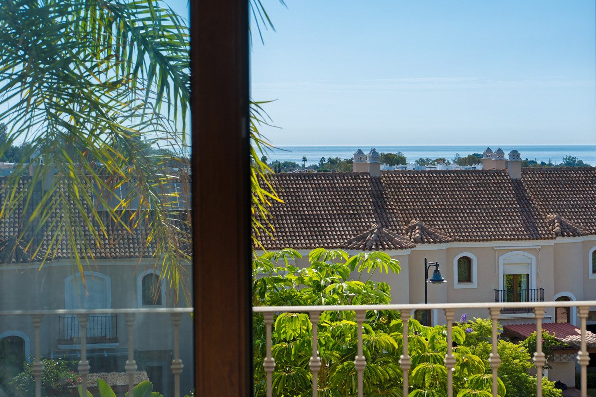View from a balcony overlooking Mediterranean townhouses with a sea view in the background and palm trees in the foreground.