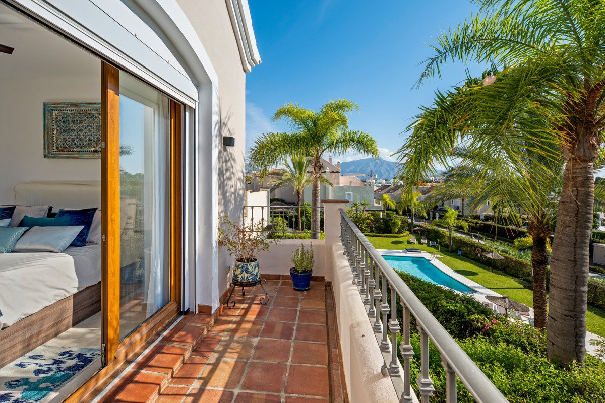 View from the balcony overlooking a swimming pool, palm trees, gardens, and distant mountains under a clear blue sky.