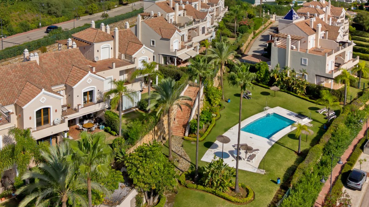 Aerial view of a luxury townhouse complex with a swimming pool, lush gardens, palm trees, and outdoor seating areas.