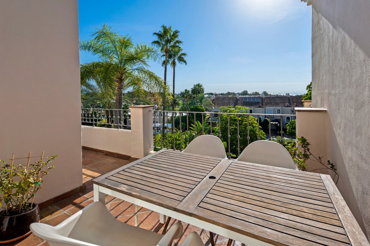 A patio with a wooden dining table and chairs overlooking a lush green landscape with palm trees and houses under a clear blue sky.