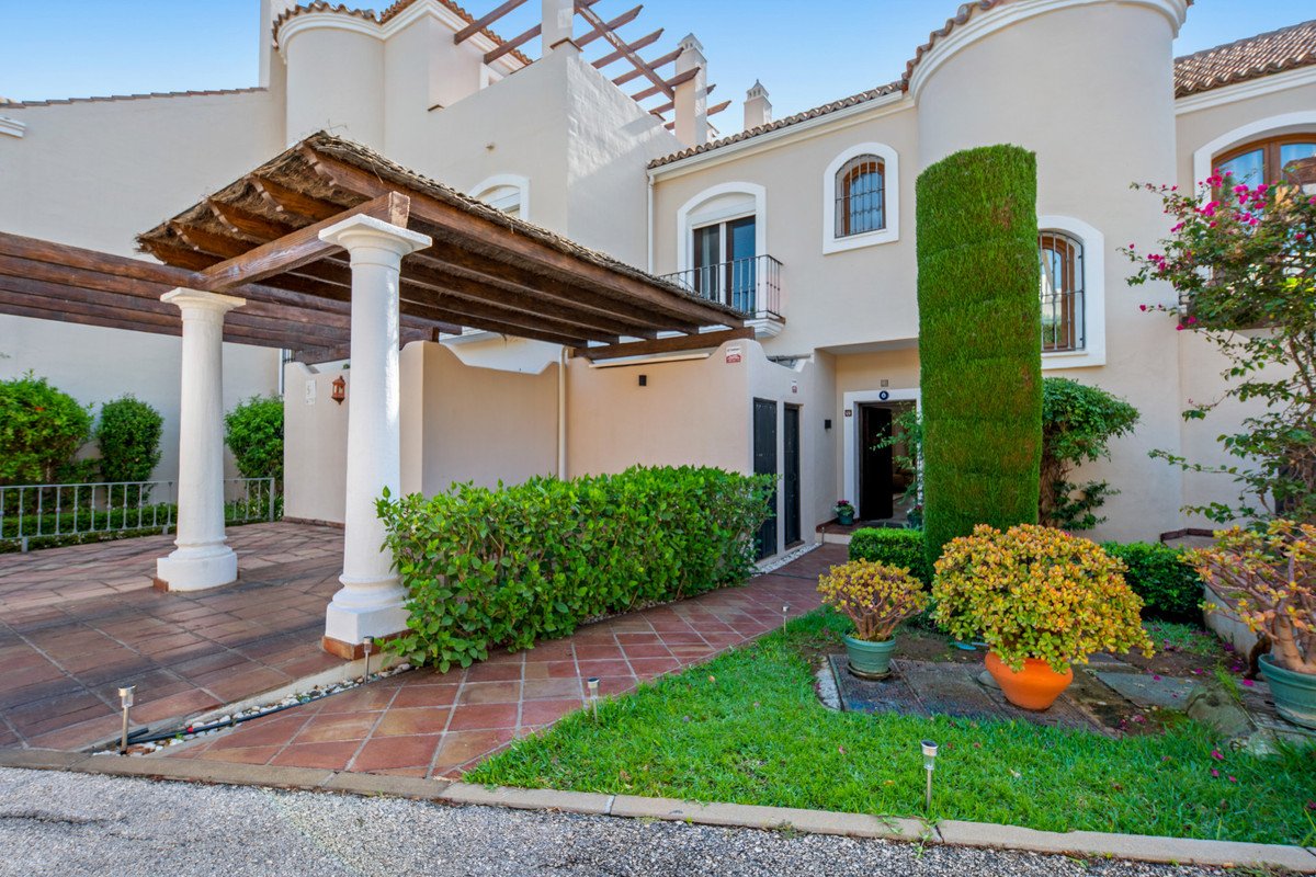 Terrace villa entrance with white pillars, wooden pergola, manicured garden, and potted plants. Mediterranean style.