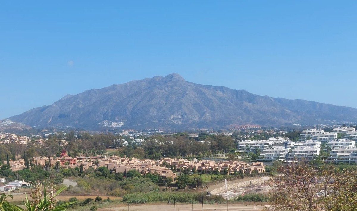 Panoramic view of apartment buildings and townhouses with a large mountain range in the background under a clear blue sky.