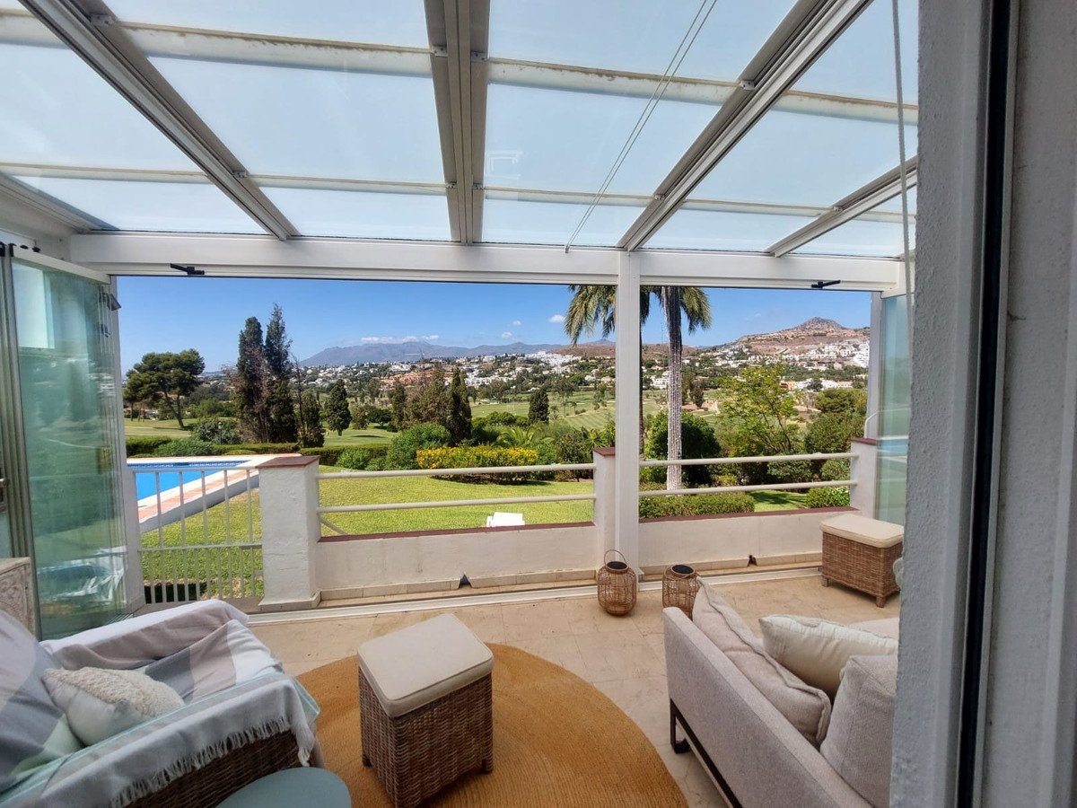 Sunroom overlooking a golf course with a swimming pool and distant hills under a clear blue sky.