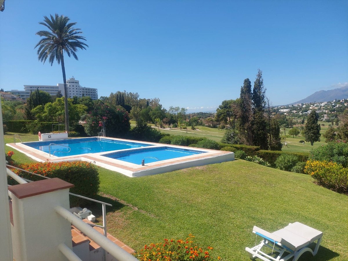 Two swimming pools with a lounge chair on a grassy lawn, overlooking a golf course and mountains under a clear blue sky.