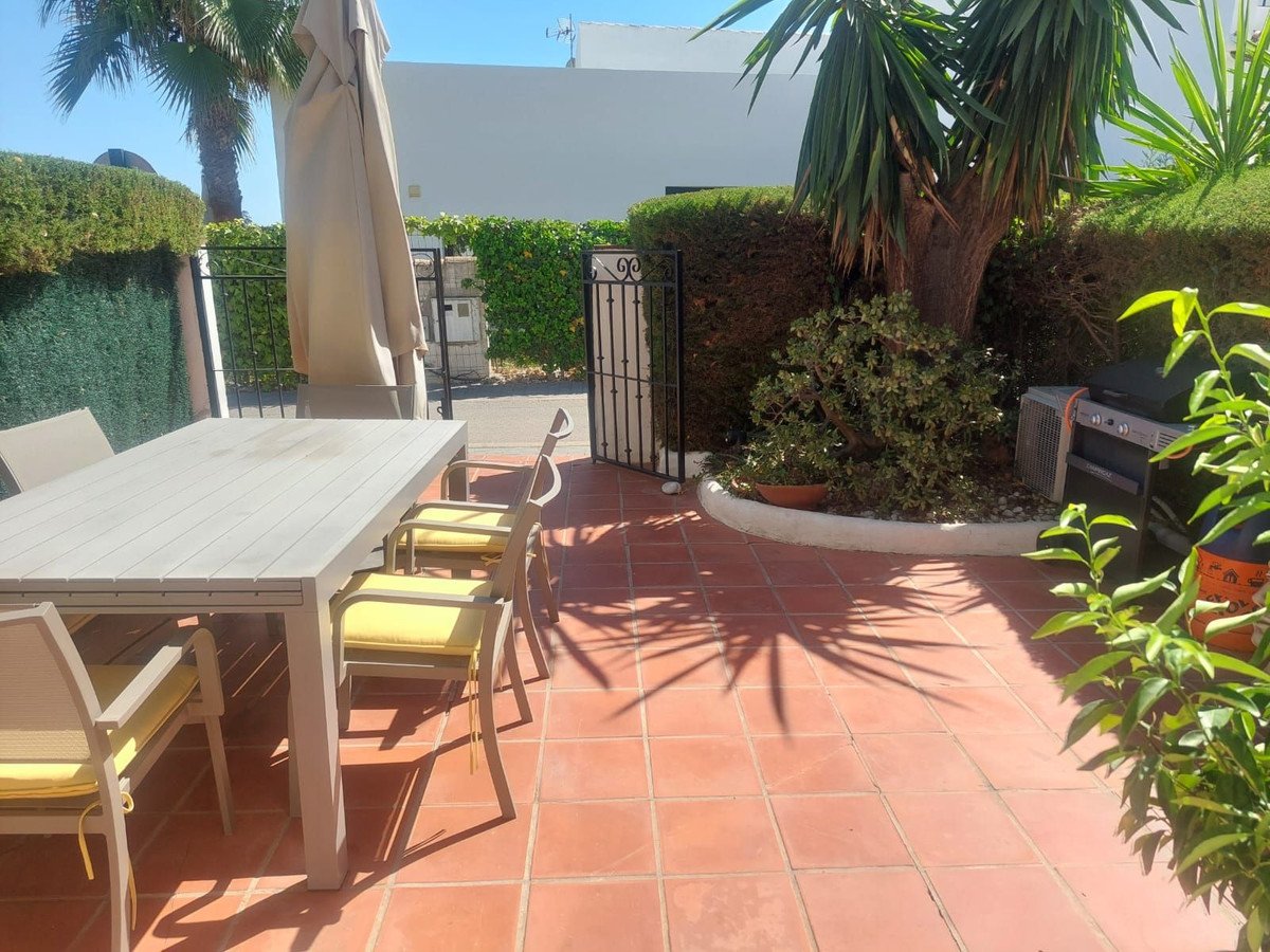 Terrace with dining table, chairs, umbrella, barbecue grill, and palm trees under a sunny sky.