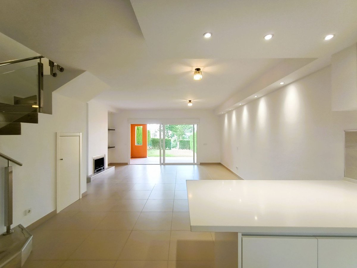 Modern open-plan living room with large windows, white walls, and tiled floor