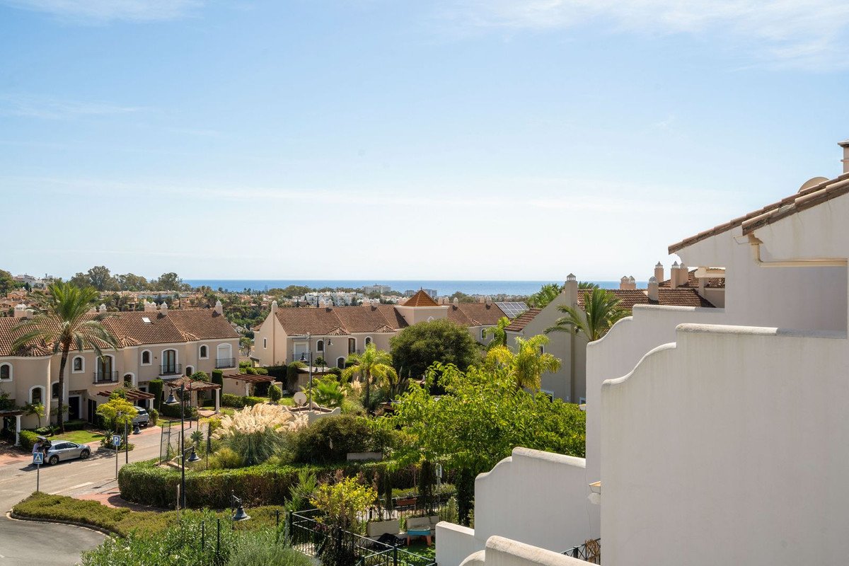 View from a terrace overlooking houses and trees with the sea visible in the distance under a clear blue sky.