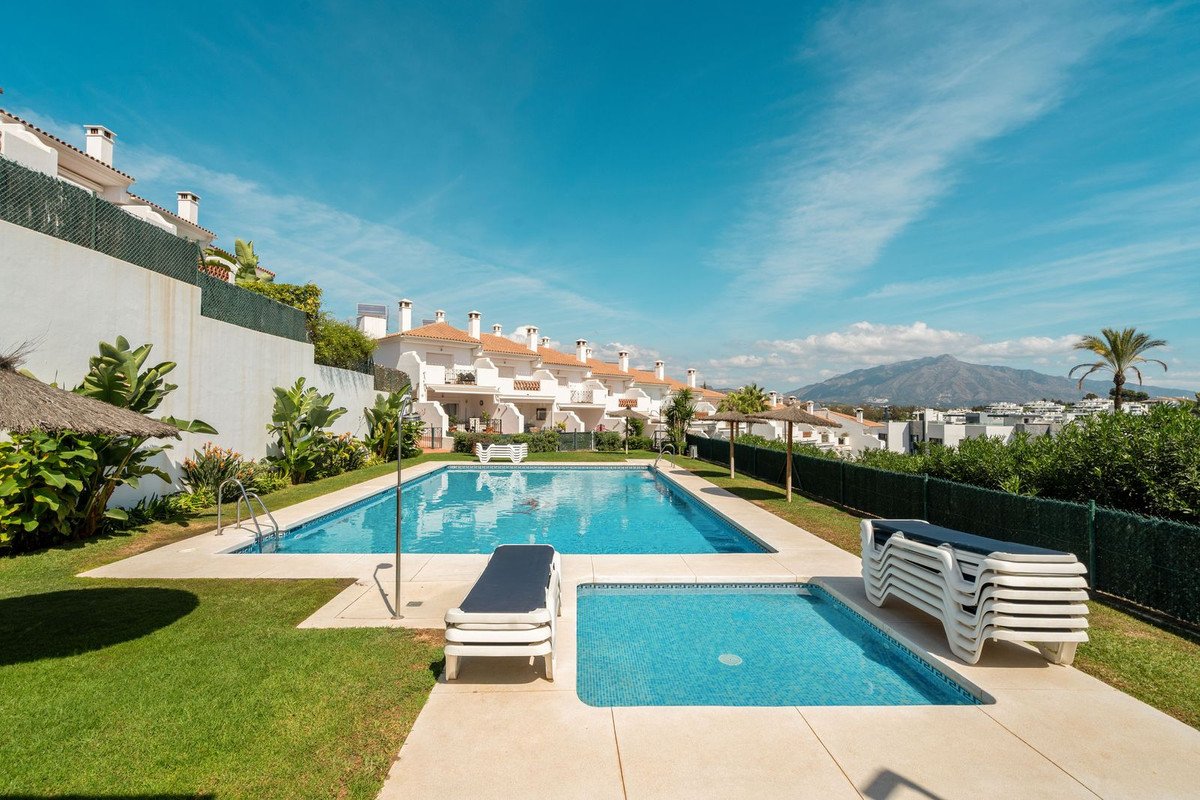 Resort-style swimming pool and lounging area with stacked chairs, overlooking residential buildings and mountains under a clear blue sky.