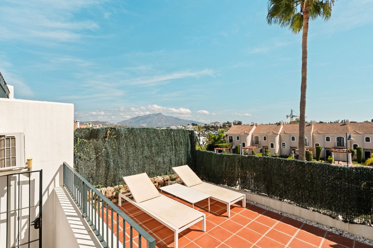 Spacious terrace with two lounge chairs and a table, offering views of mountains and neighboring houses.