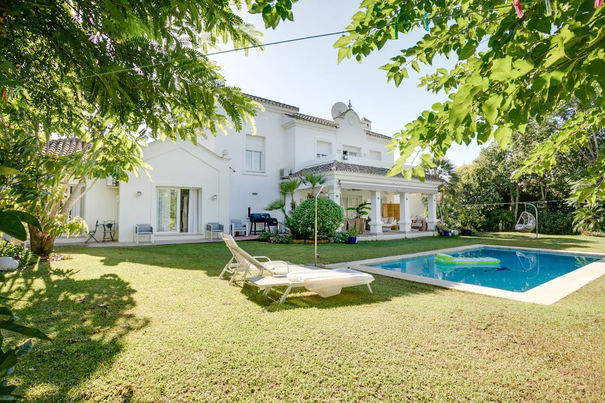A white villa with a swimming pool, lounge chairs, and a lush green garden, perfect for outdoor relaxation.
