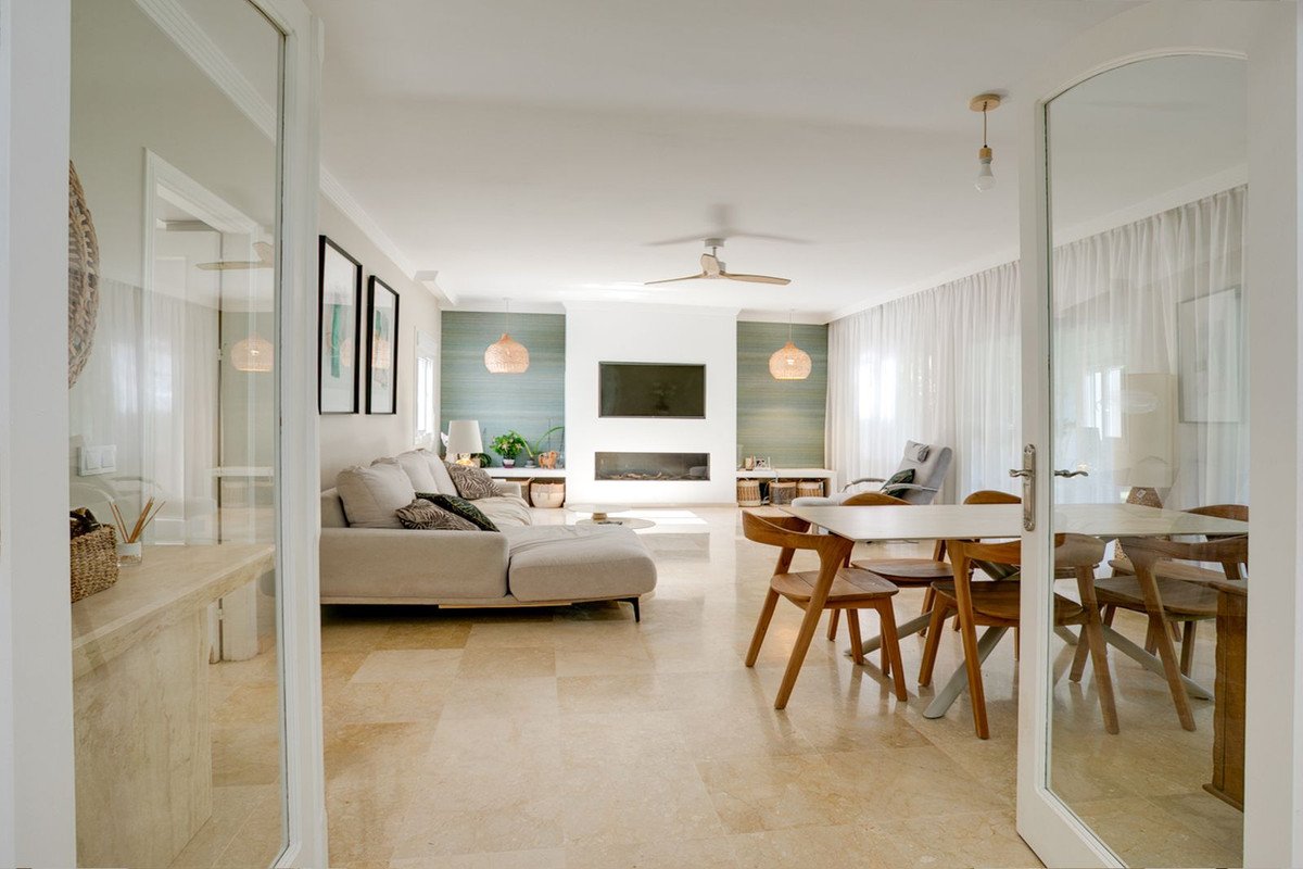 Spacious living and dining area with modern furniture, fireplace, and natural light streaming through sheer curtains.