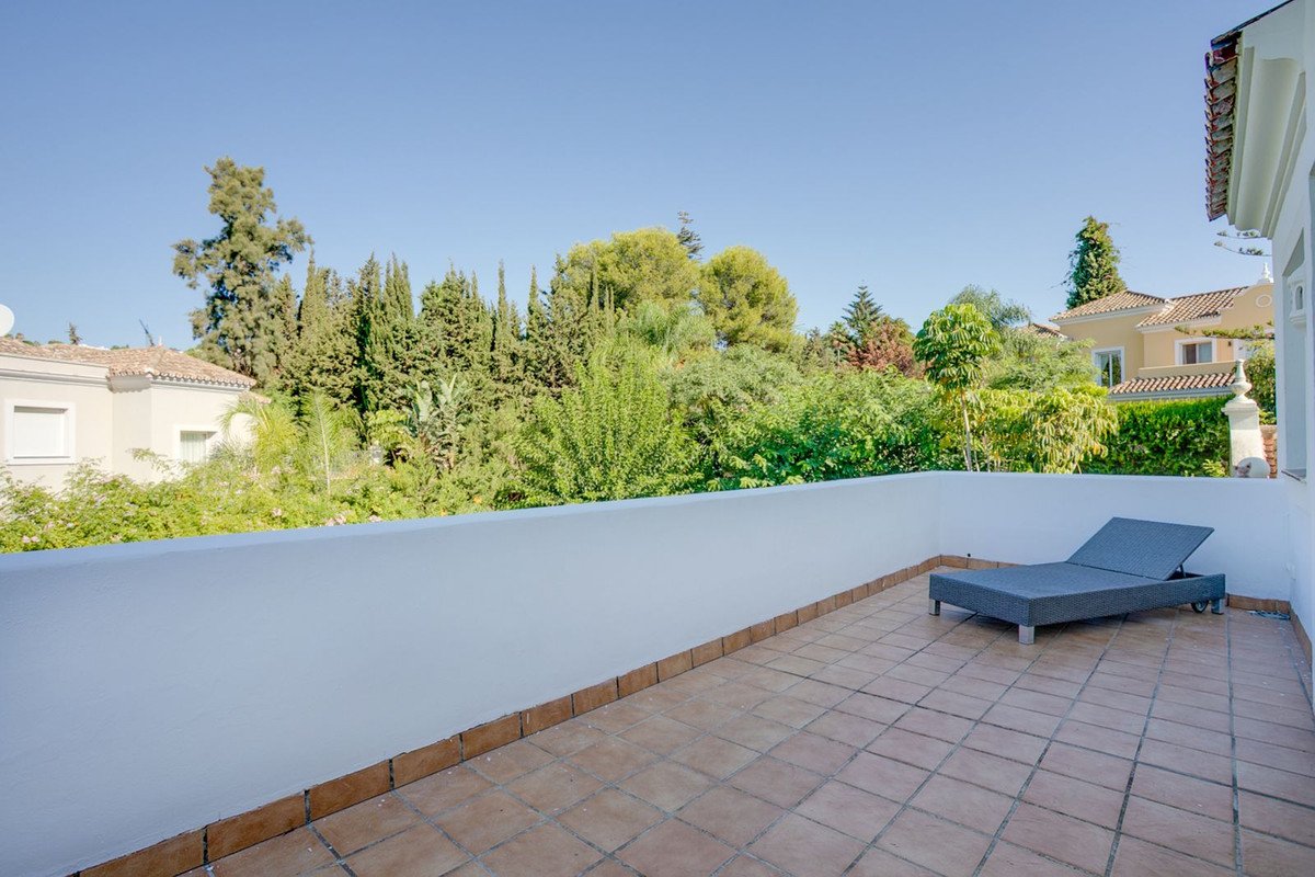 A spacious tiled terrace with a gray lounge chair offering a peaceful view of lush green trees and a bright blue sky.
