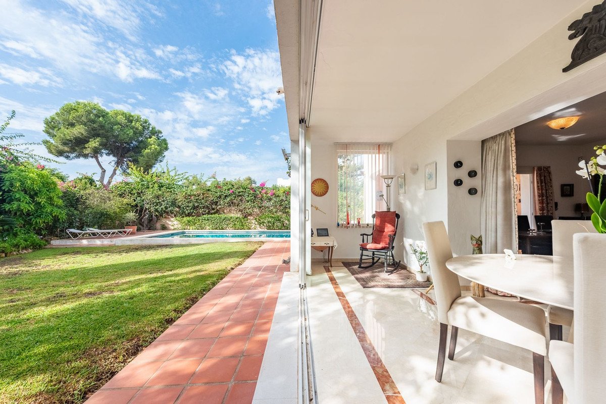 Modern patio with dining area and rocking chair, overlooking a lush garden with a swimming pool.