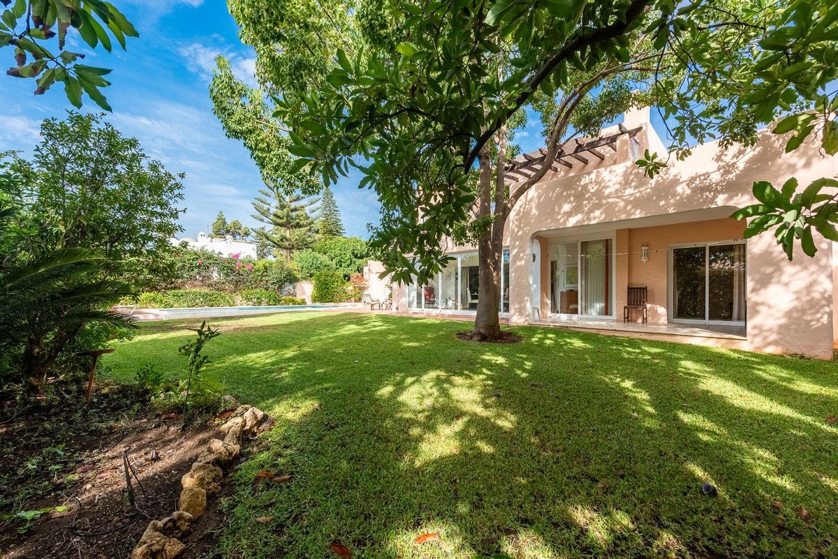 Spacious green garden with a swimming pool, patio with large sliding doors, and mature trees providing shade.