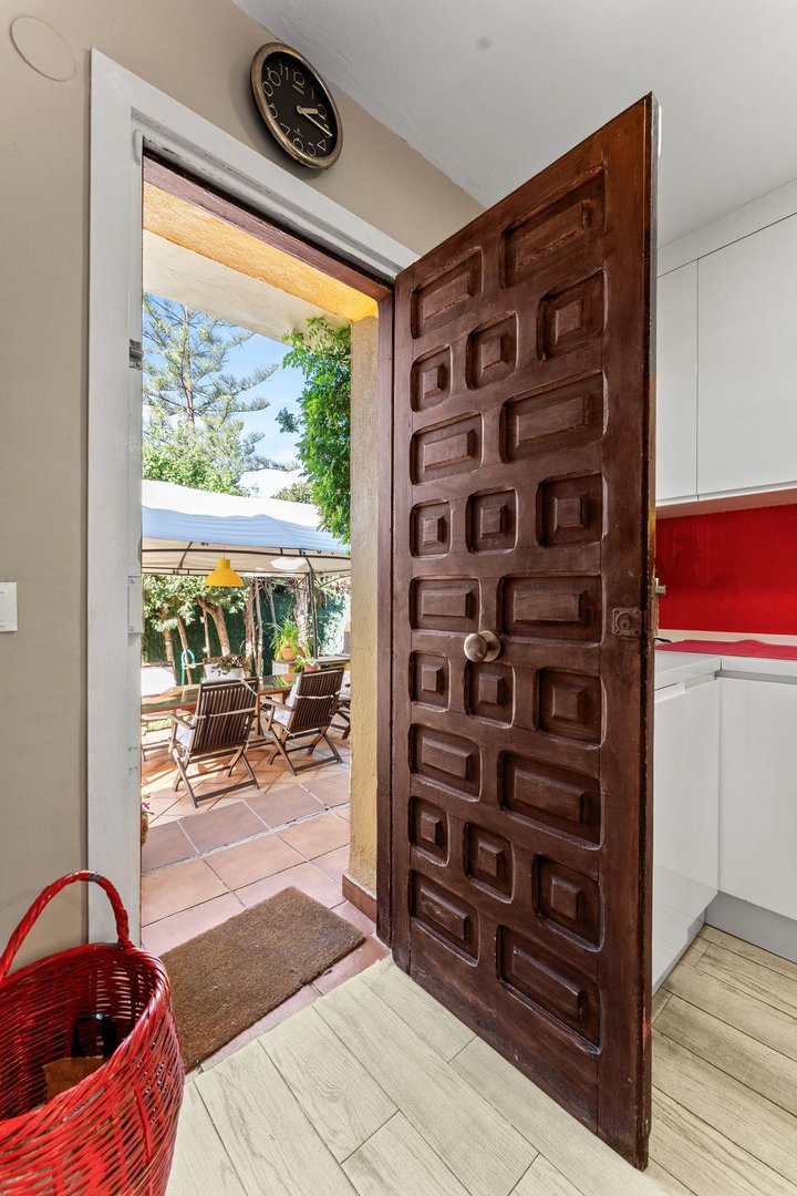 View of a terrace with chairs and a table through an open wooden door with a red basket in the foreground.
