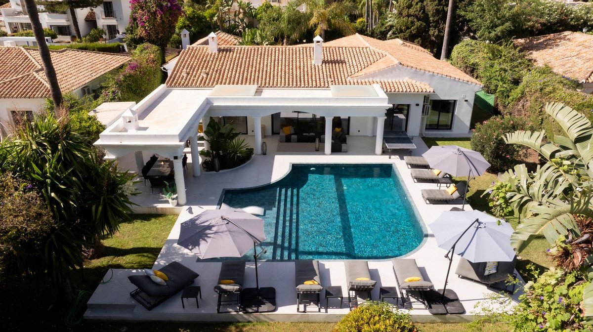 Luxury villa with a large blue swimming pool, sun loungers, umbrellas, and a covered outdoor lounge area.