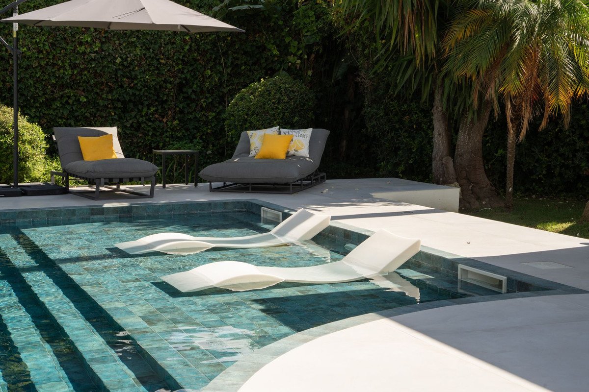 A pool with white loungers, outdoor seating with yellow cushions, and a large umbrella.