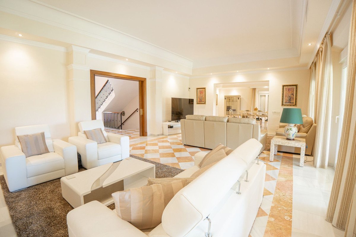 Spacious living room with beige sofas, chairs, a coffee table, and a view into a dining area and staircase.