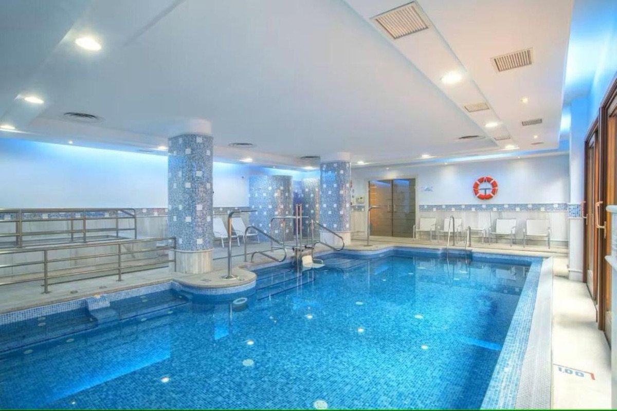 Indoor swimming pool with blue water, tiled columns, and seating area