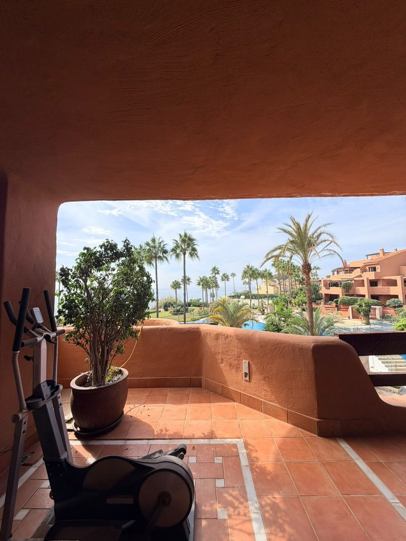 Balcony with exercise bike, potted plant, and view of pool, palm trees, and resort buildings