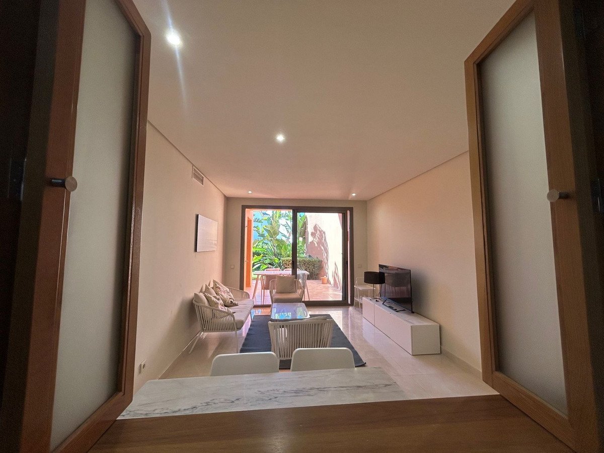 Modern living room with white furniture, large windows opening to a lush terrace with tropical plants and seating.