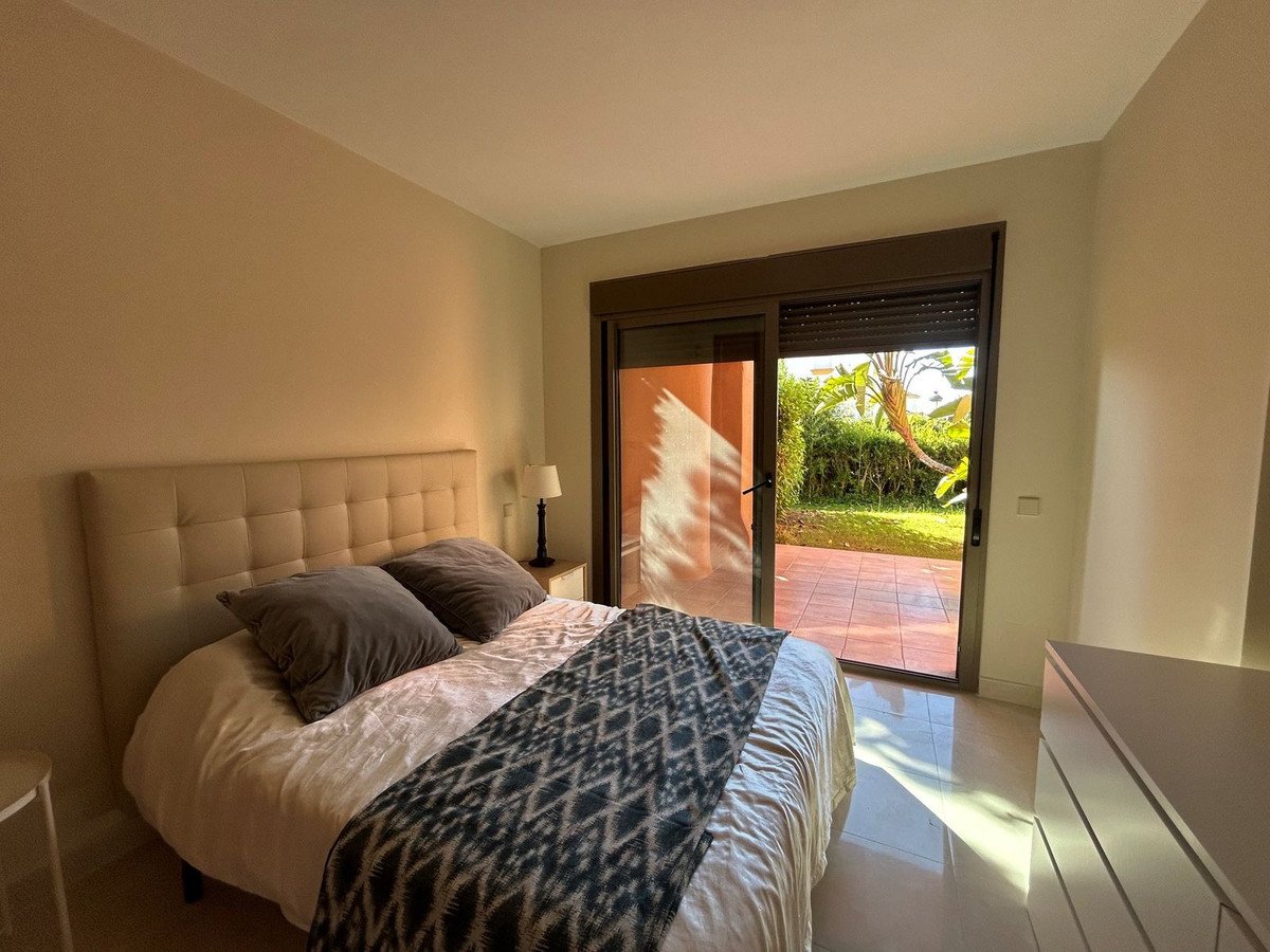 Bedroom with queen-size bed and patterned throw, leading to a patio and garden through glass sliding doors.