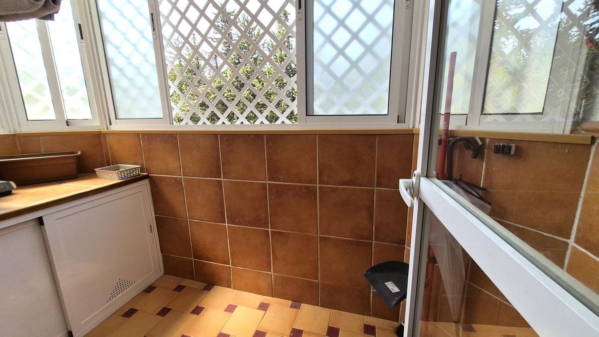 Sunlit utility room with tiled walls, wooden countertop, and lattice window view.