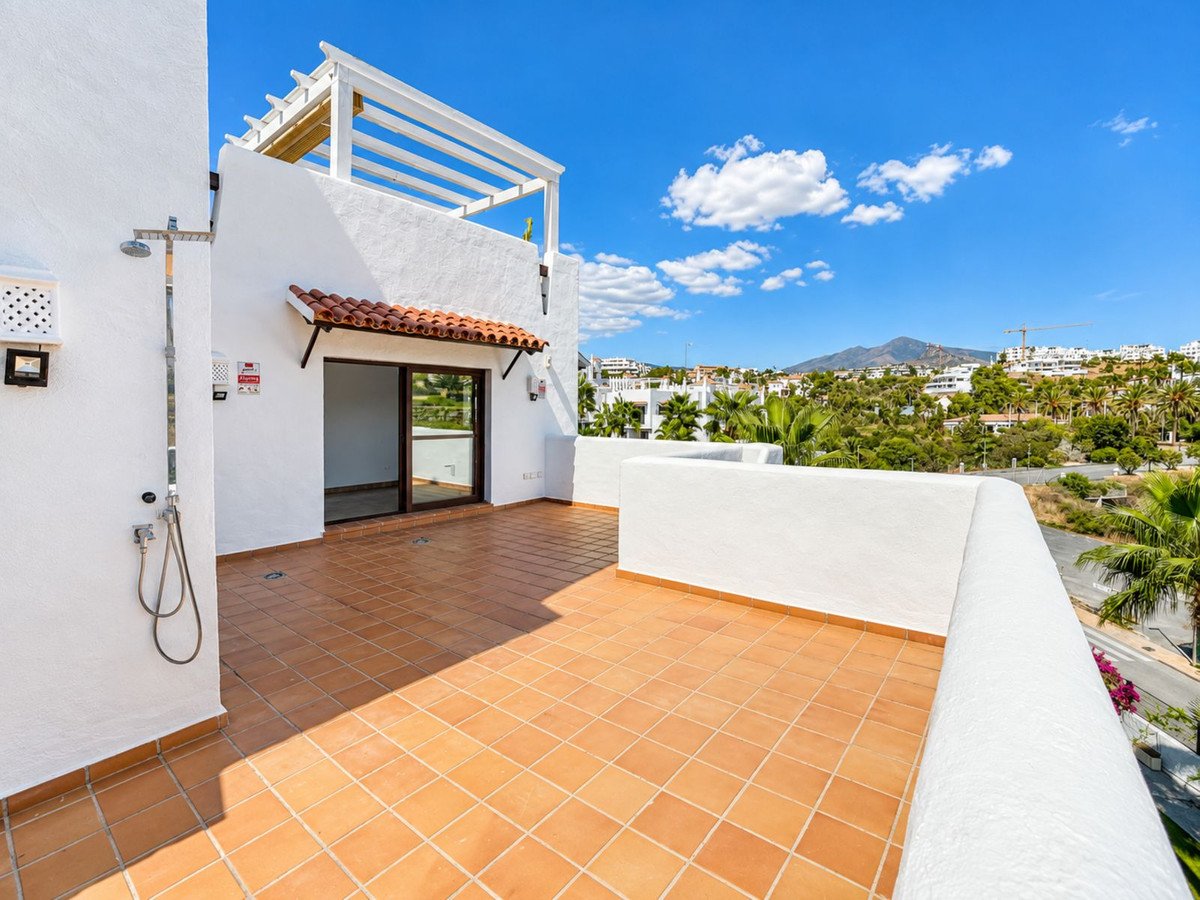 Spacious tiled terrace with an outdoor shower and a view of mountains and palm trees under a blue sky.