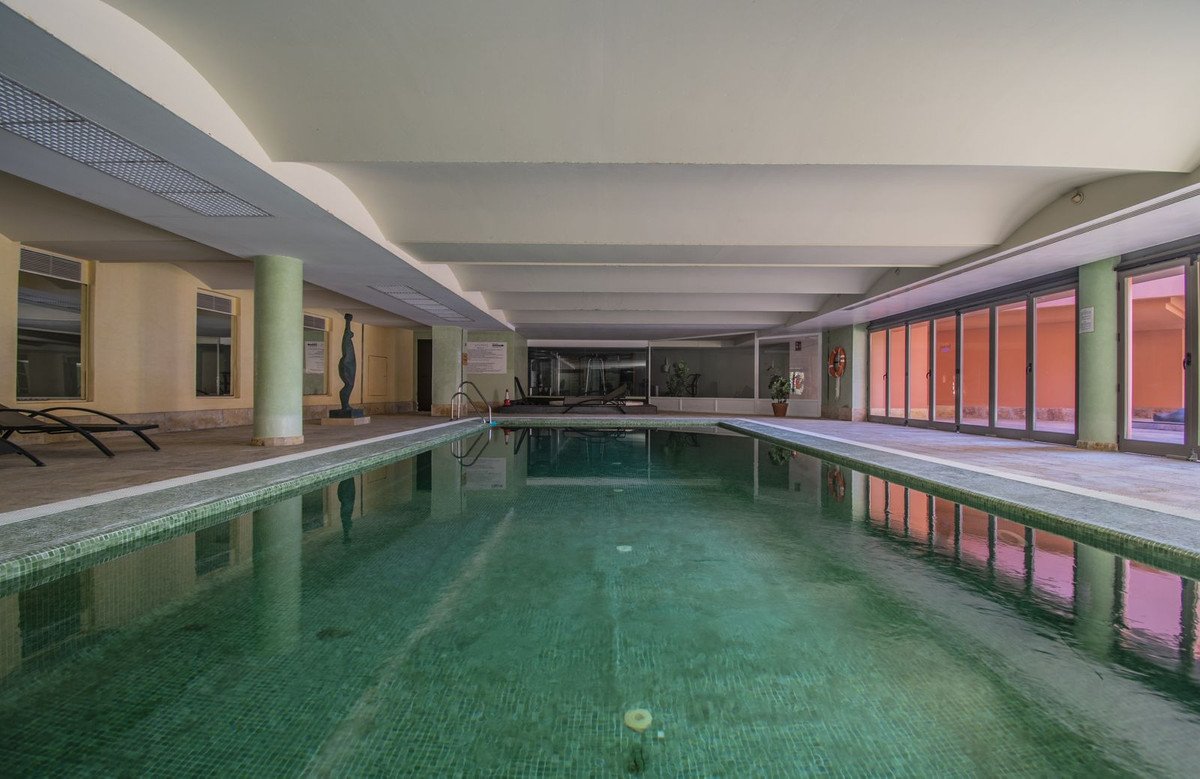 Indoor swimming pool with tiled edges, lounge chairs on the side, and large glass doors reflecting the outdoor light.