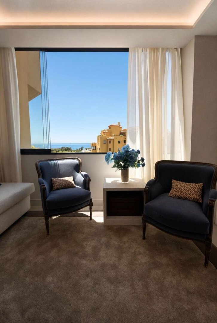Living room with ocean view, two blue armchairs, and a side table with flowers