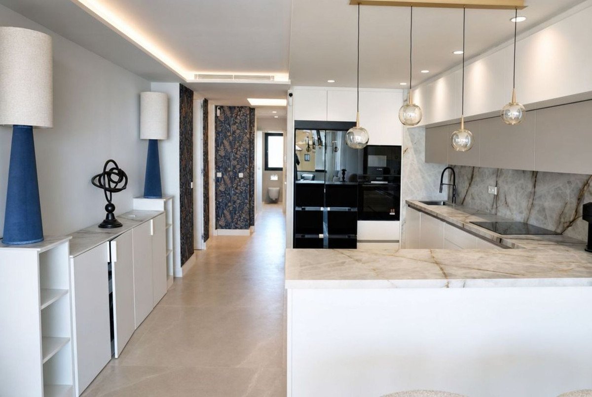 Modern kitchen and living room with marble countertops, pendant lights, and sleek cabinetry.
