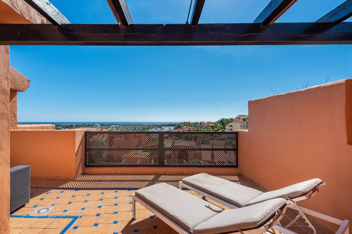 A sunny terrace with lounge chairs, tiled flooring, and a sea view beyond the railing.