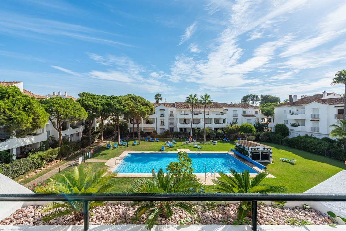View of a large blue swimming pool and manicured lawn surrounded by white apartment buildings and lush green trees.