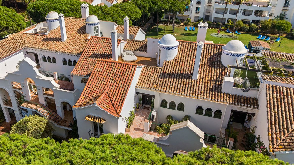Aerial view of a white villa with tiled roofs, balconies, garden, and swimming pool in the background.