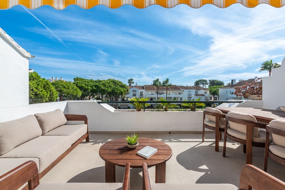 A spacious terrace with modern outdoor furniture, including a sofa and dining set, offering a view of buildings and trees.
