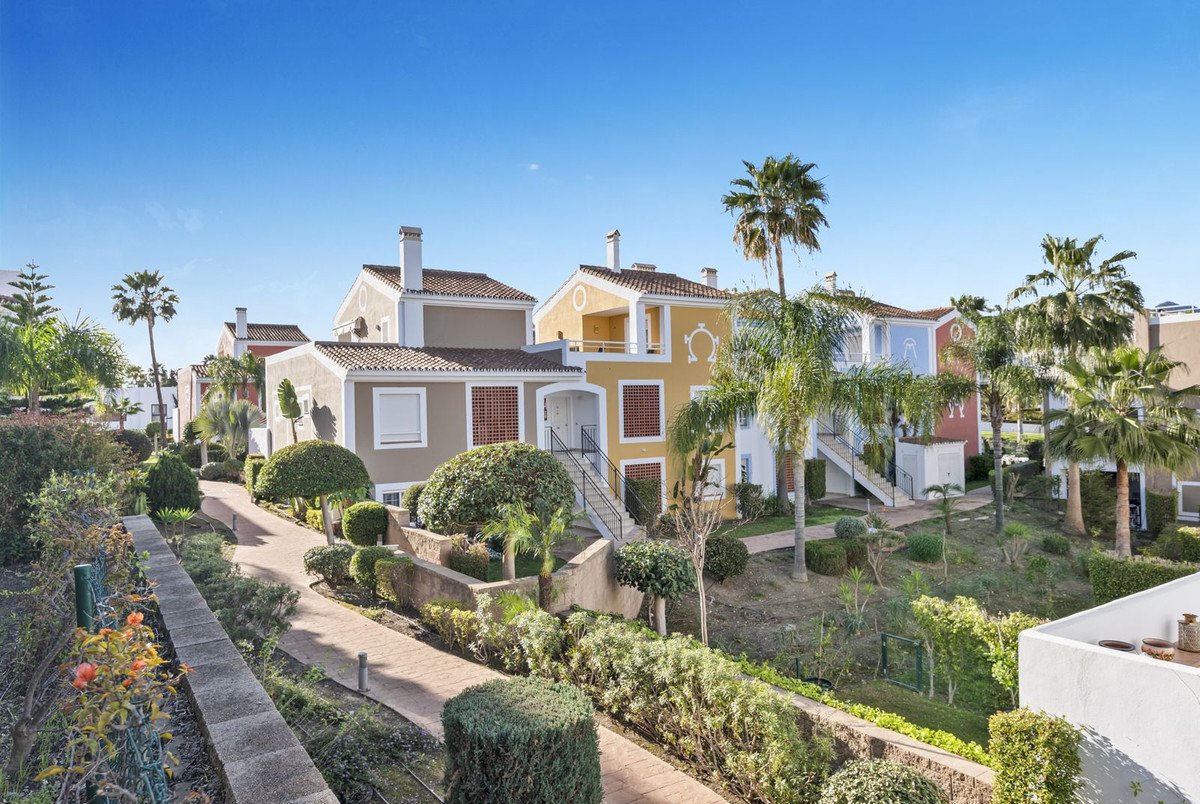 Colorful townhouses with tropical gardens and palm trees under a clear blue sky.