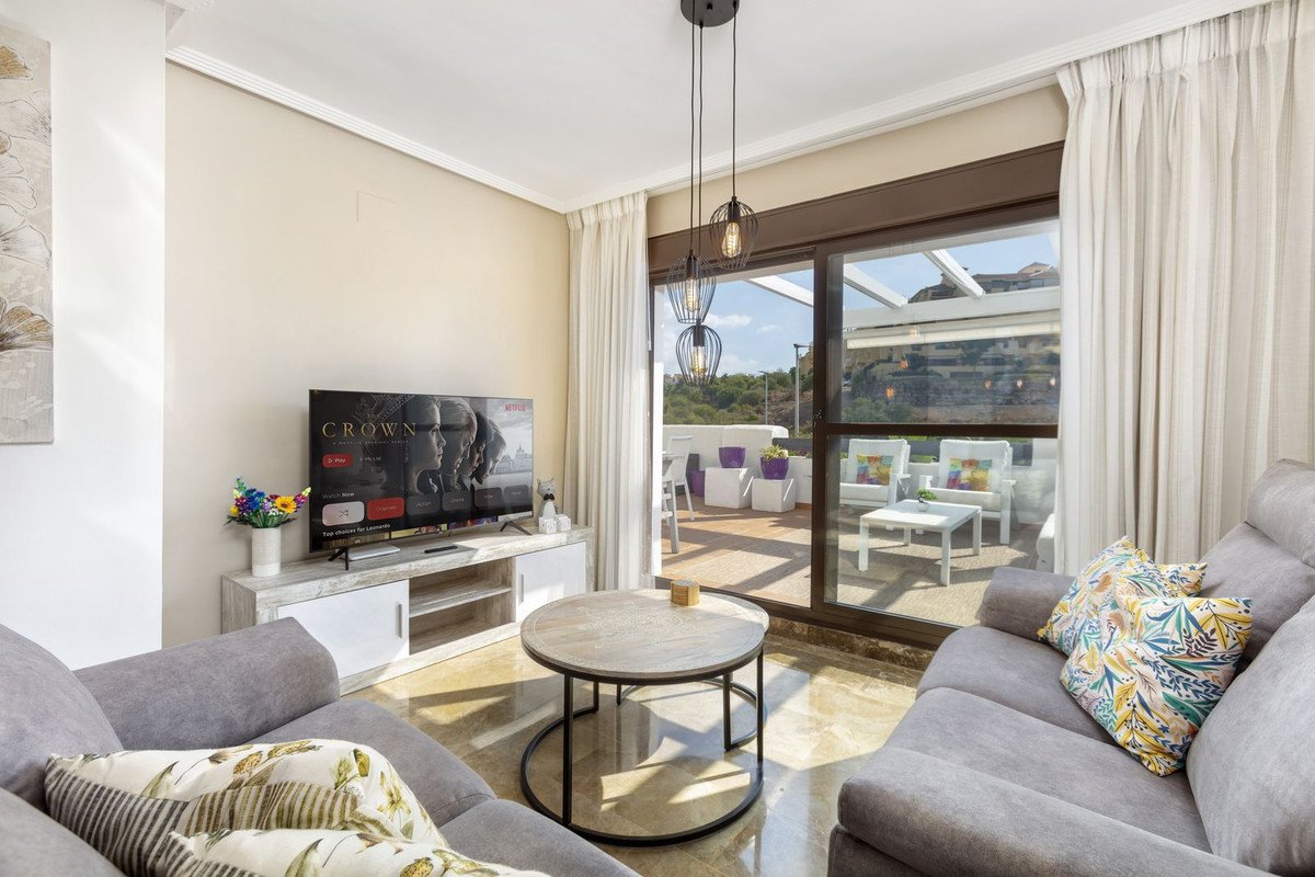 Modern living room with comfortable sofas, coffee table, TV, and sliding doors opening to a terrace with outdoor seating and views.