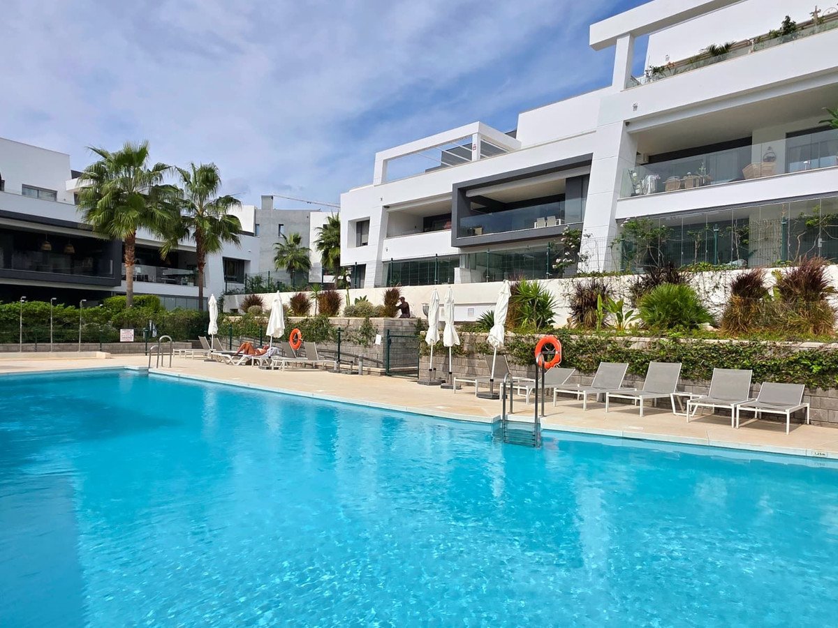 Outdoor swimming pool area with lounge chairs and modern apartments in the background, surrounded by palm trees and greenery.